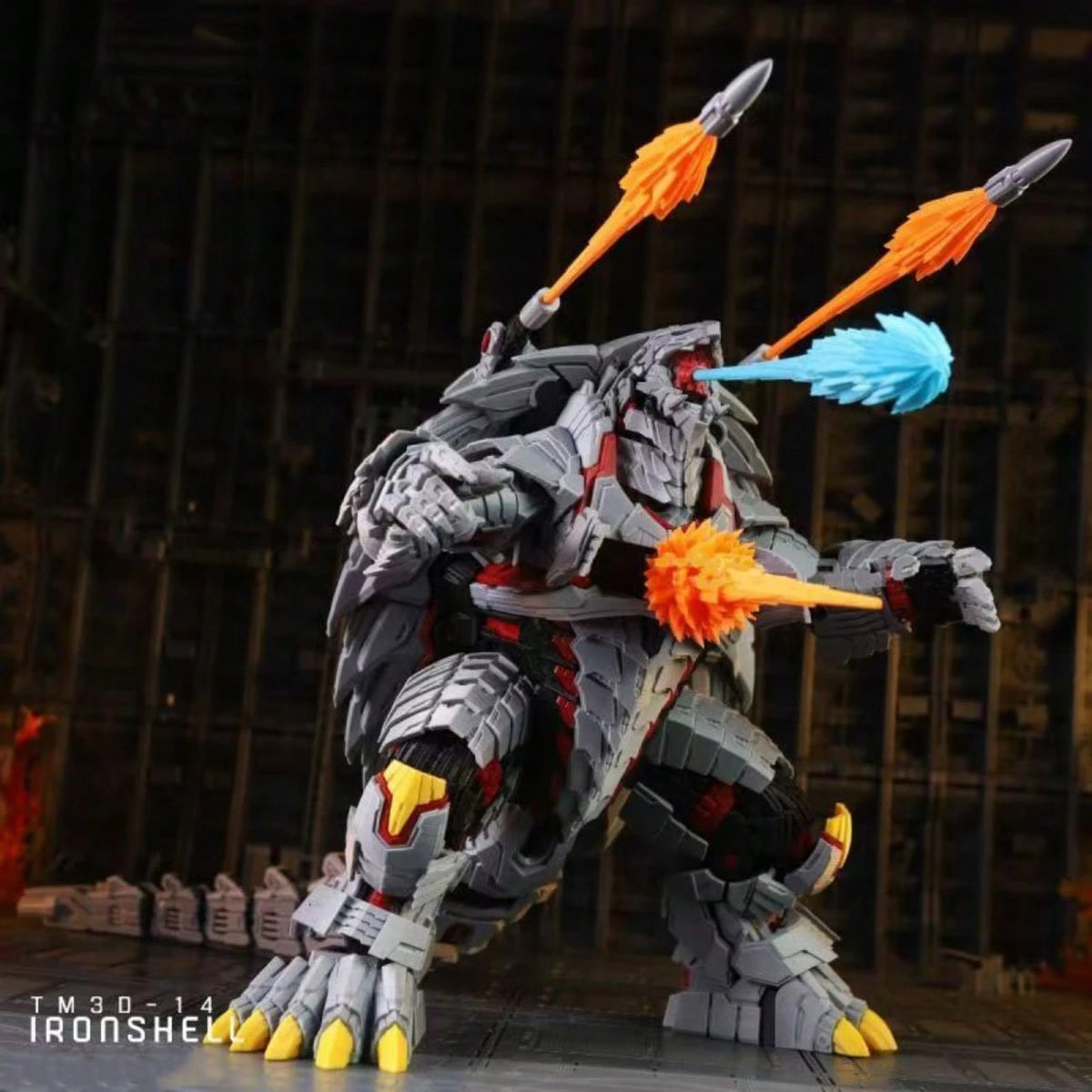 A detailed toy model of a robotic monster, resembling Ironshell from Gears of War, in a dynamic battle stance. The model is primarily gray with black and red armor plating, yellow claws, and carries orange and blue energy weapons.