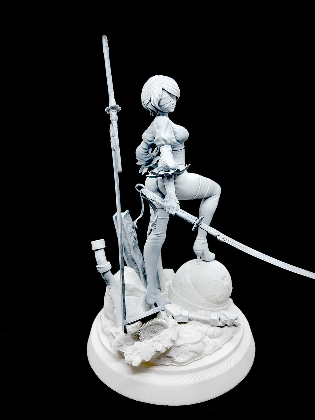 An unpainted white resin figurine of a female anime character in a combat pose, holding a sword and standing on a detailed round base against a solid black background.