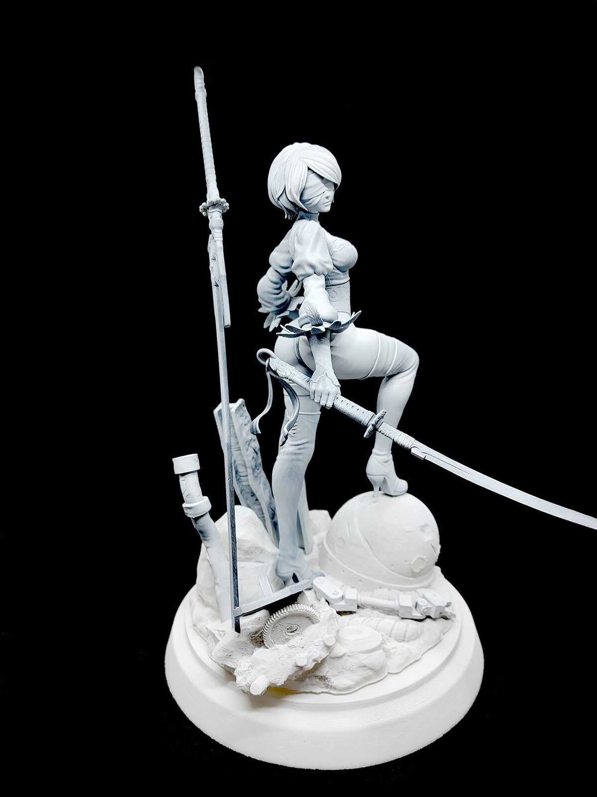 An unpainted white resin figurine of a female anime character in a combat pose, holding a sword and standing on a detailed round base against a solid black background.