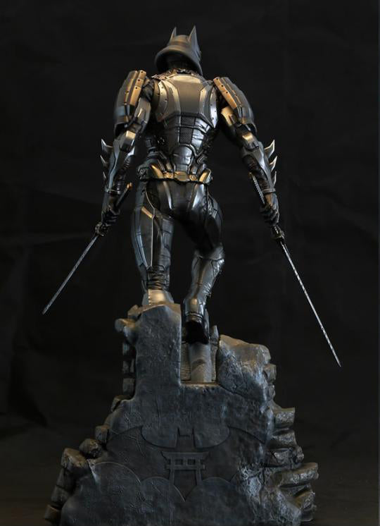A Batman armored statue in dark metallic armor, standing on a rocky base and holding two swords, photographed against a black background.