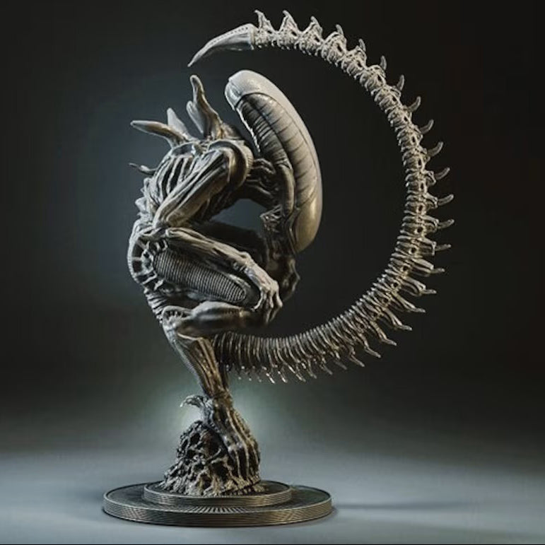 A detailed sci-fi creature statue resembling an Alien Xenomorph, posed in a crouched stance with a long curved spine-like tail arching overhead, mounted on a circular base against a dark studio background.