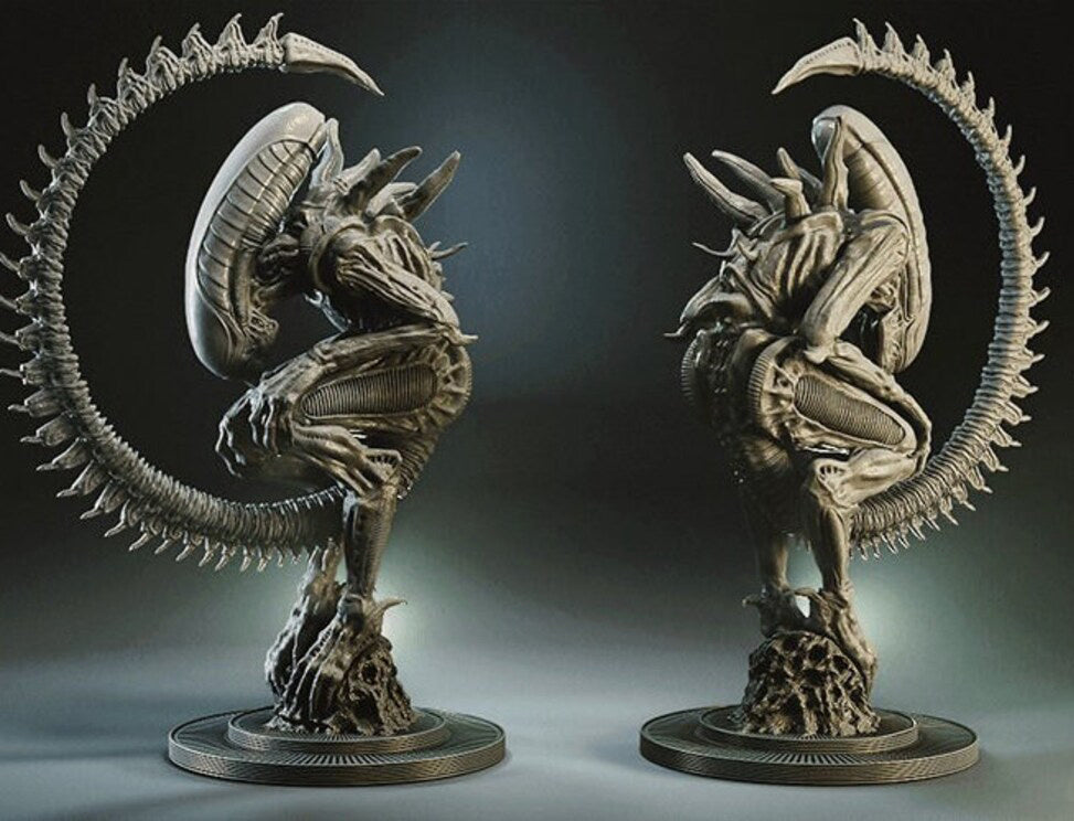 Two identical detailed sci-fi creature figurines posed facing each other, shown on a dark studio background. The creatures have metallic gray bodies with a large curved spiky tail and are mounted on round bases.