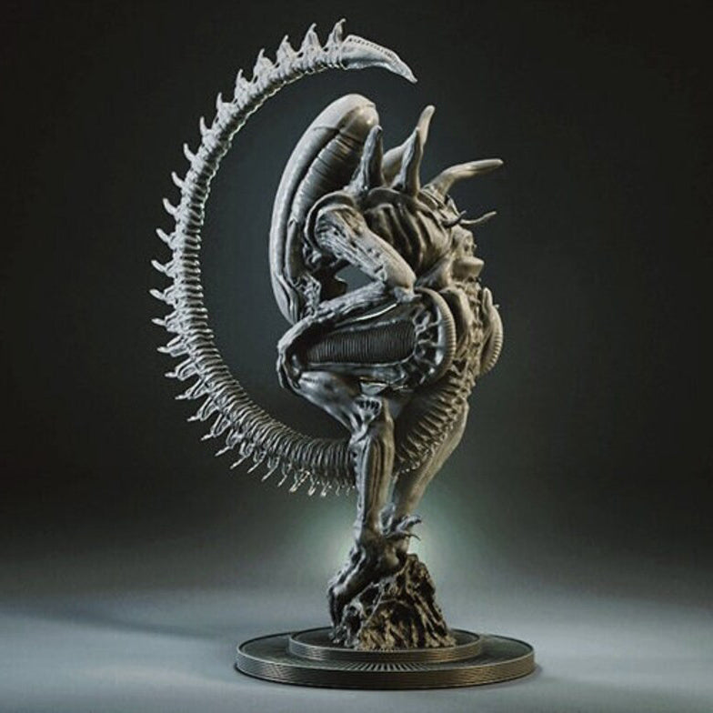 A detailed sci-fi creature statue in a crouched pose with a long curved tail, shown on a circular base against a dark studio background.