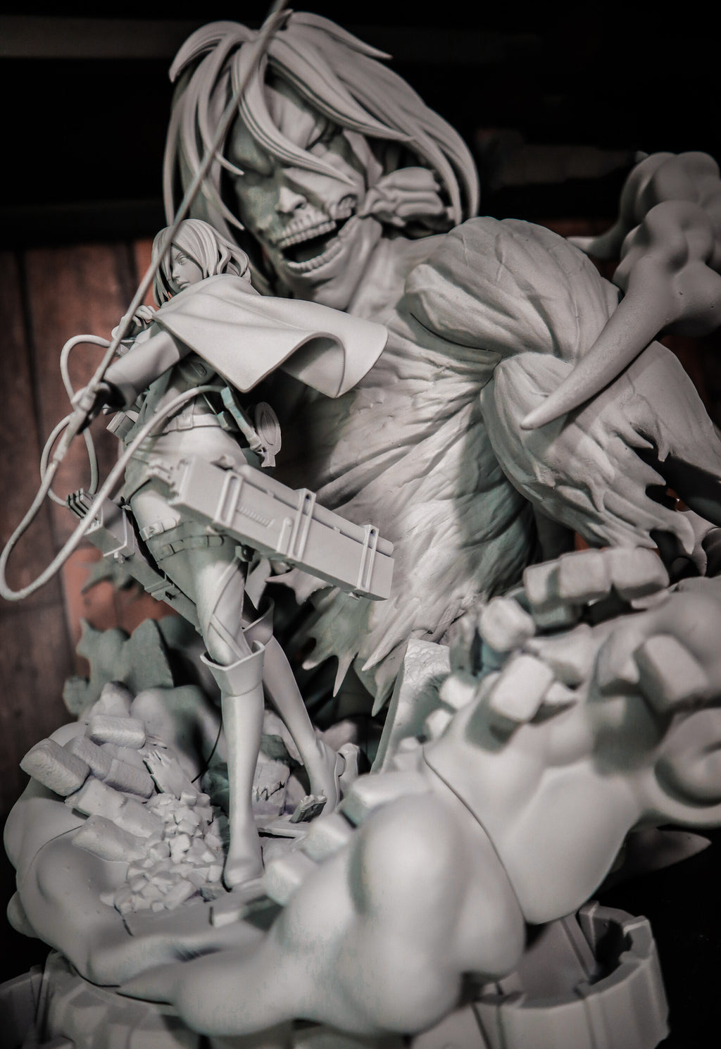 A monochrome gray resin statue depicting a dynamic battle scene with two anime-style characters amidst rubble, photographed in a dark indoor setting.