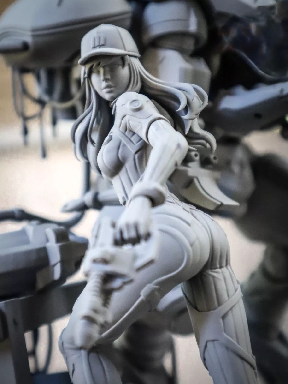 Gray-scale figurine of a woman with long hair and a helmet, sitting on a mechanical or futuristic background.