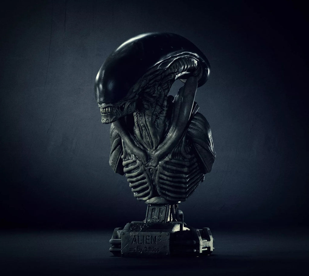 A dark metallic bust sculpture of an Alien Xenomorph on a pedestal base, photographed against a moody dark gray studio background.