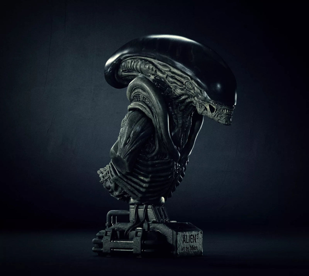 A dark, highly detailed bust sculpture of an Alien Xenomorph on a textured base, photographed in dramatic low-key lighting against a dark studio background.