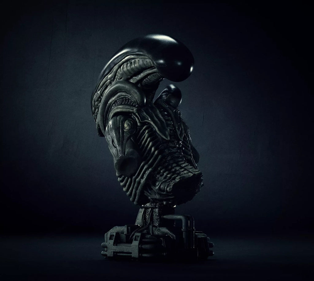 A dark, highly detailed sci-fi creature bust sculpture on a pedestal, photographed in dramatic low-key lighting against a dark studio background.