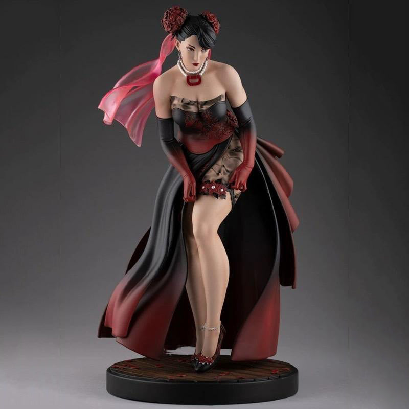 Statue of a woman in a red and black outfit with a flowing cape on a gray background