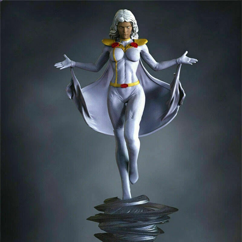 A detailed collectible statue of a female superhero character with white hair, wearing a white bodysuit with yellow and red accents and a flowing white cape, posed on a dark metallic base against a dark gray gradient background.