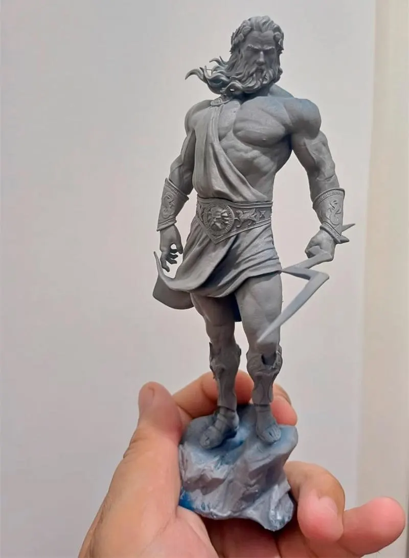 Gray statue of Zeus held by a hand against a plain background