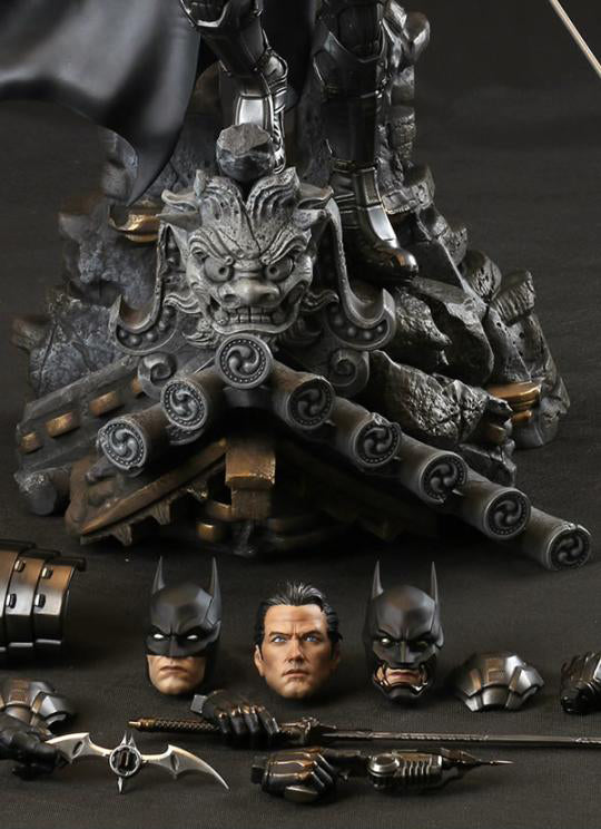 A detailed Batman collectible figure and base set displayed on a dark surface, featuring a large ornate gothic base with a dragon head, multiple interchangeable Batman faces, armor pieces, a cactus weapon, and other accessories.