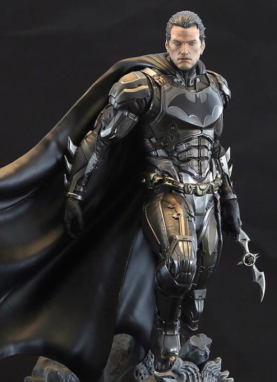 A highly detailed collectible action figure of Batman in a dark armored suit with a flowing black cape, posed dynamically against a dark studio background.