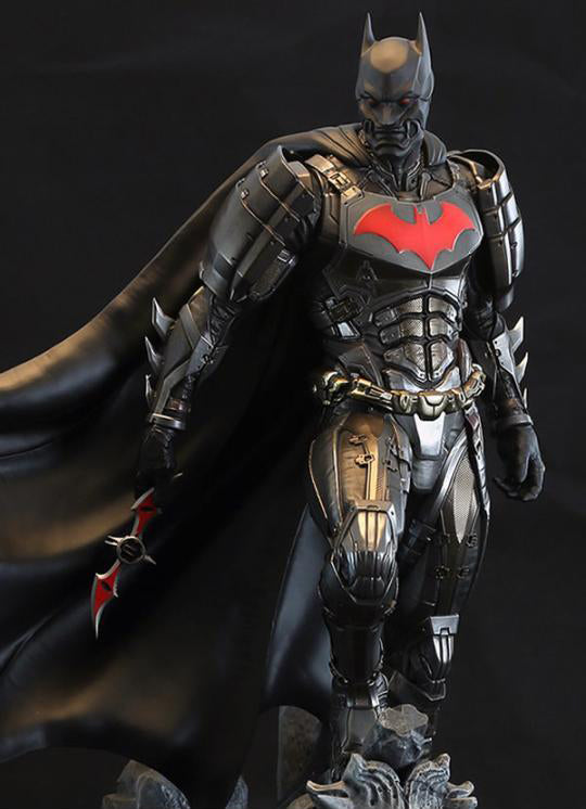 A highly detailed Batman armored collectible figure in dark metallic armor with a flowing black cape, standing against a dark studio background. The chest features a prominent red bat symbol, and the figure is posed with one arm extended holding a red-and-black bat-shaped object.