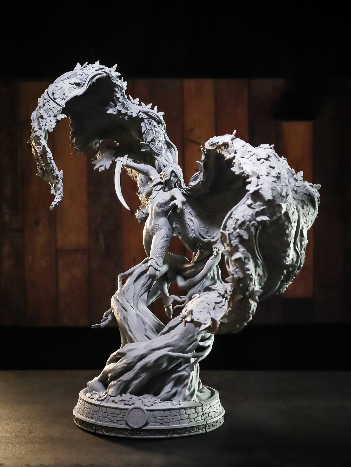 A detailed fantasy sculpture of a warrior figure emerging from swirling, cloud-like forms, mounted on a circular base, photographed against a dark wood-paneled background.