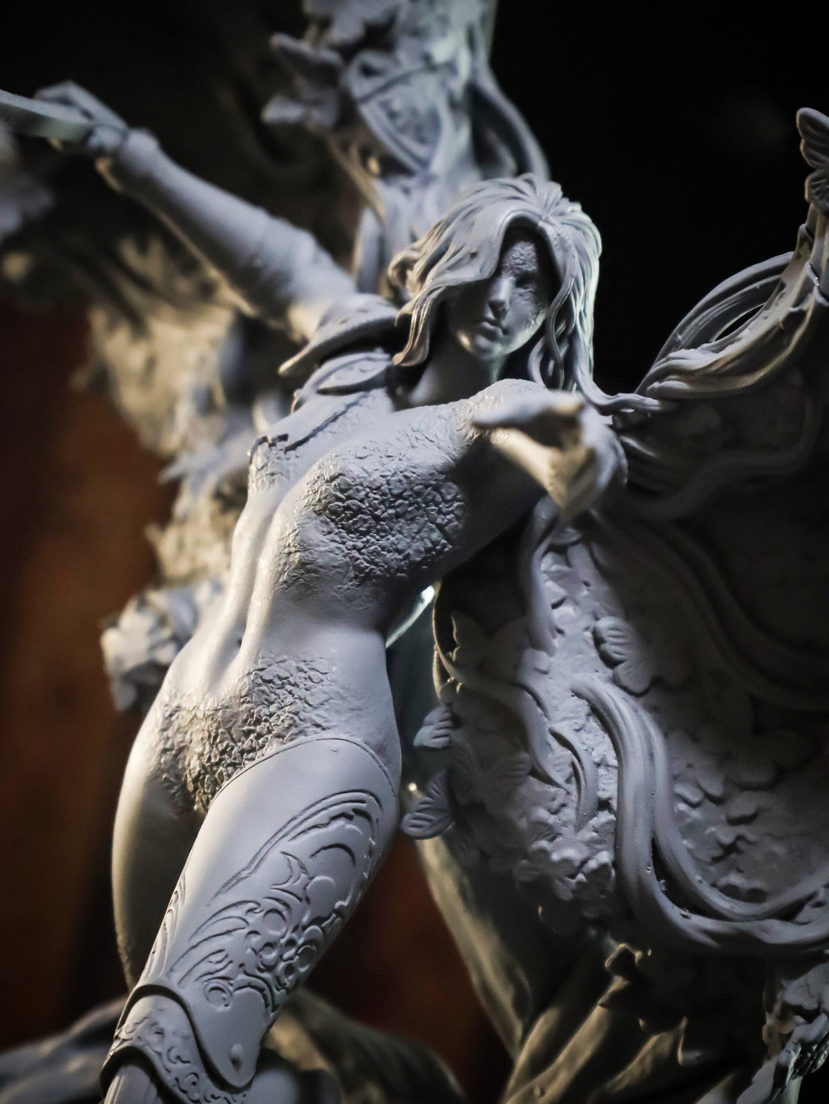 A close-up of a detailed gray resin or 3D-printed fantasy figurine depicting a female warrior in armor with a winged creature, set against a dark background.