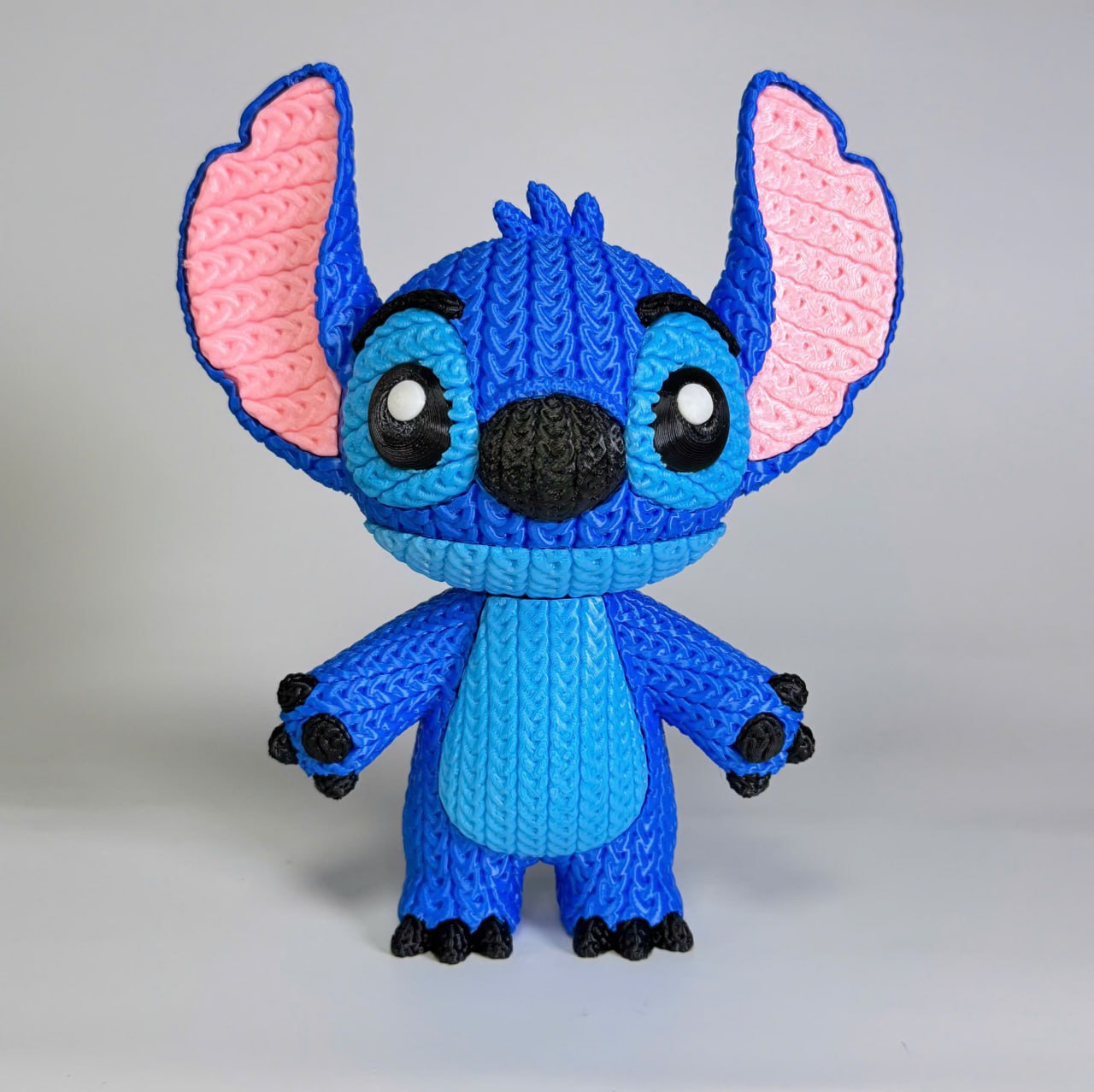 Blue plush stitch toy with pink ears on a gray background
